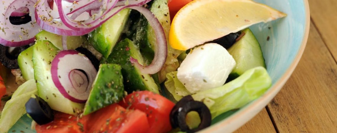 A vibrant bowl of Greek salad with fresh vegetables, feta cheese, and a lemon slice.