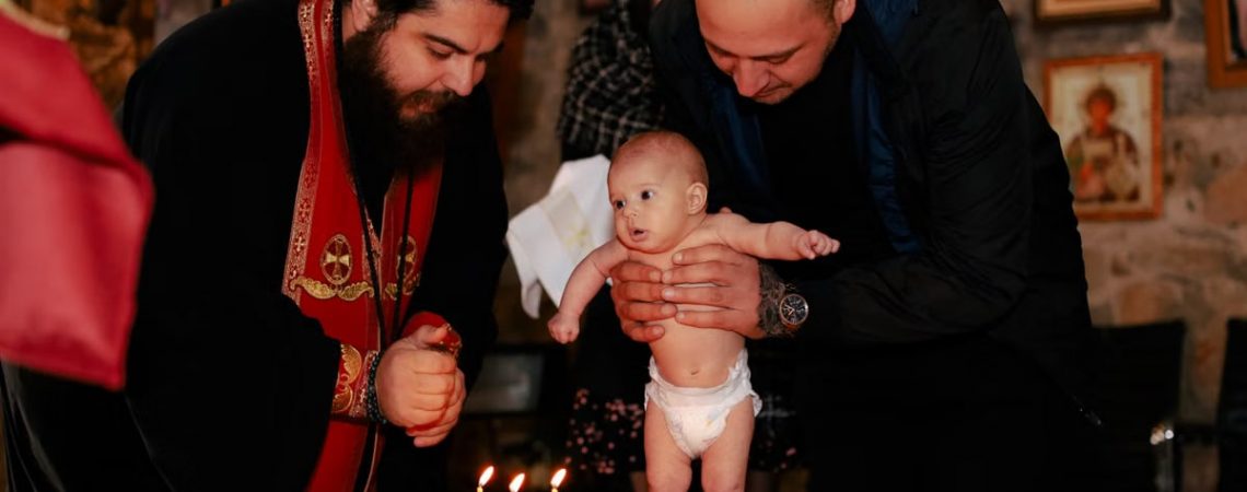 A priest and father performing an Orthodox baptism ceremony with a baby.